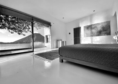 Room One at Anzan Atitlán with a stunning view of Lake Atitlán and volcanoes through expansive glass windows, featuring minimalistic design and abundant natural light.