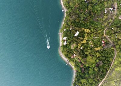 Aerial view of Anzan Atitlán on the lakeshore, overlooking Lake Atitlán’s clear blue waters with a boat crossing.