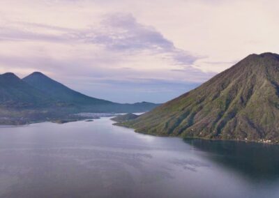 Aerial view of Lake Atitlán with San Pedro Volcano and lush green mountains under a serene sky.