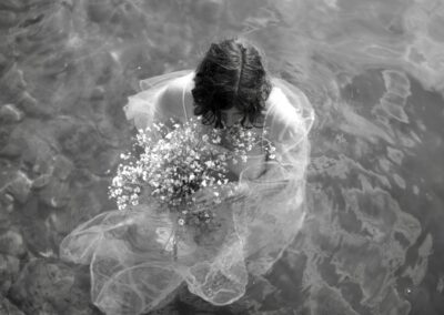 Bride in sheer white gown floating in Lake Atitlán, holding baby's breath bouquet, photographed from above in black and white, intimate lakefront wedding at Anzan Atitlán, San Marcos La Laguna, Guatemala.
